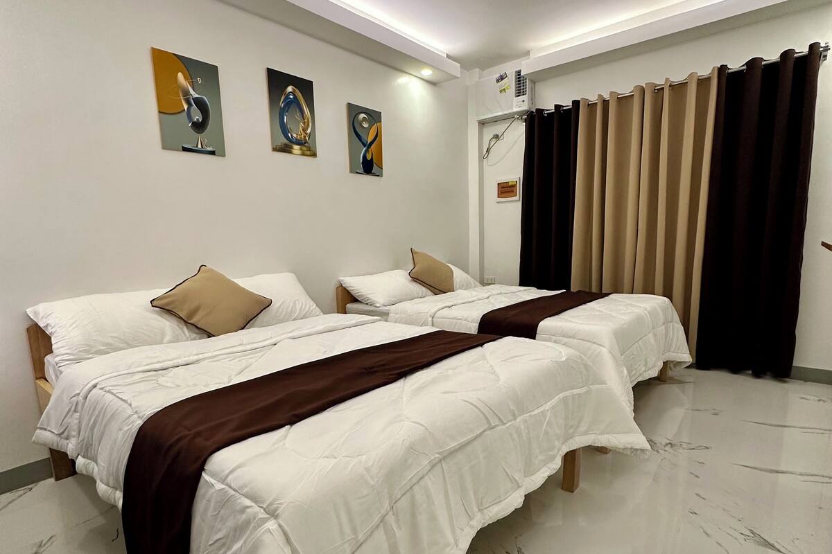 Quarto de hotel com três camas de solteiro, piso de mármore e arte abstrata nas paredes.