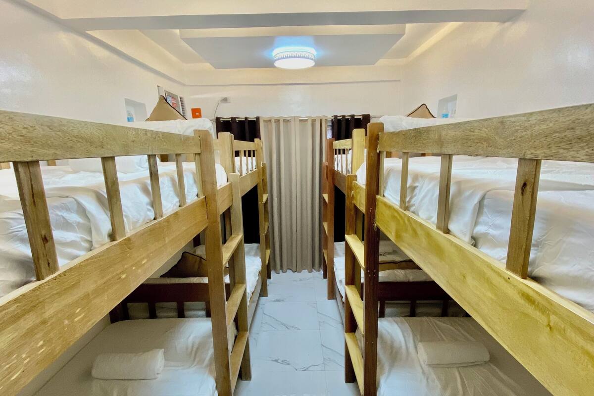 Quarto com beliches, um corredor central e um lustre no teto.