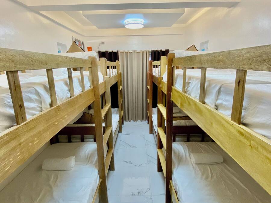 Una habitación con literas, un pasillo central y una lámpara en el techo.