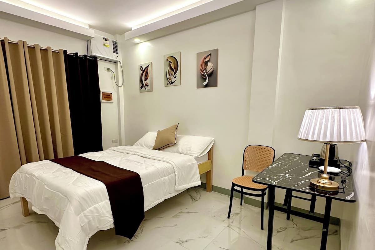 Quarto de hotel moderno com uma cama, uma mesa com cadeira e uma luminária.