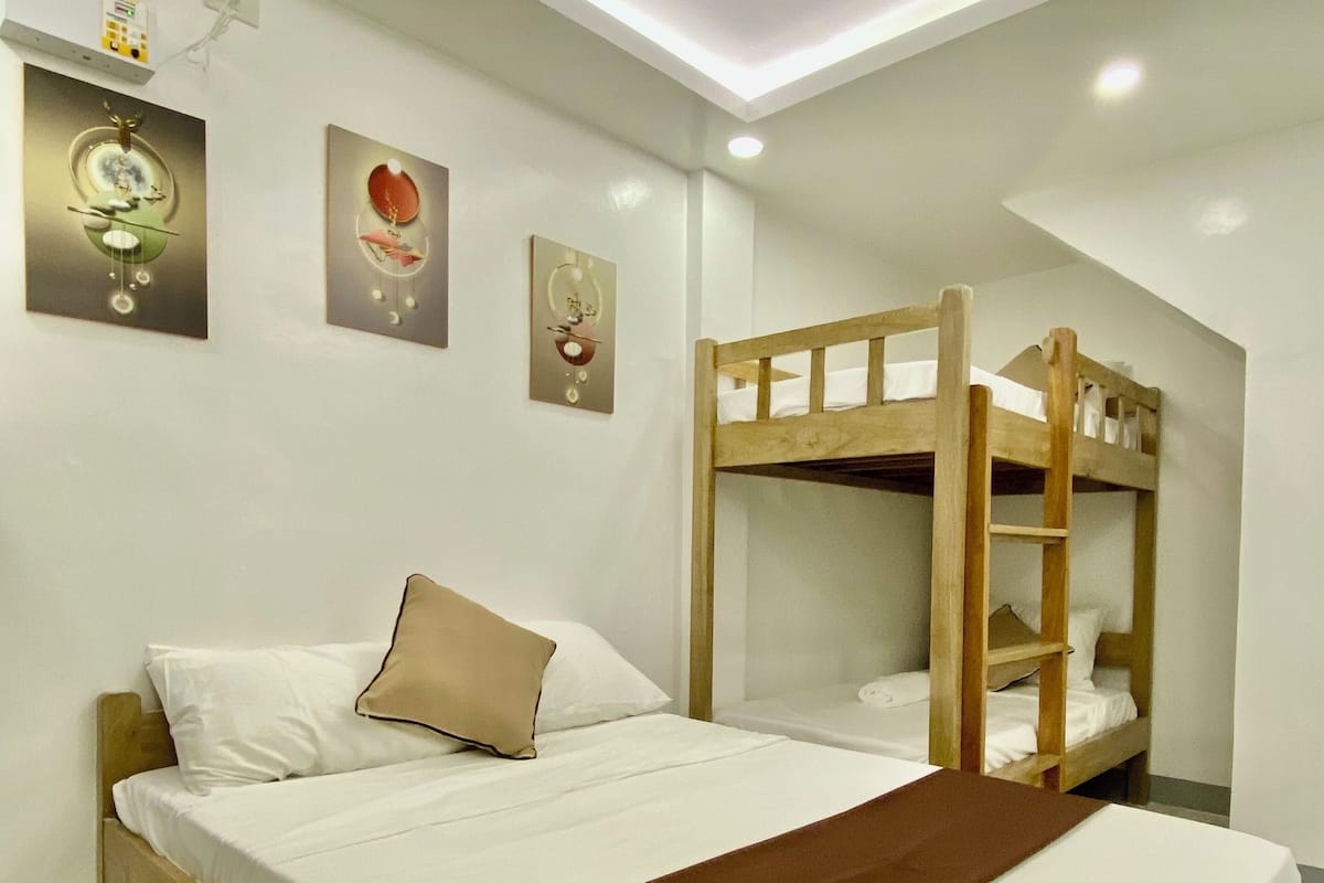 Quarto com cama beliche, uma cama de solteiro, roupa de cama branca, manta marrom e decoração nas paredes.