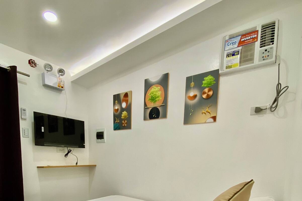 Quarto com cama de madeira, roupa de cama branca, televisão montada na parede e obra de arte pendurada.