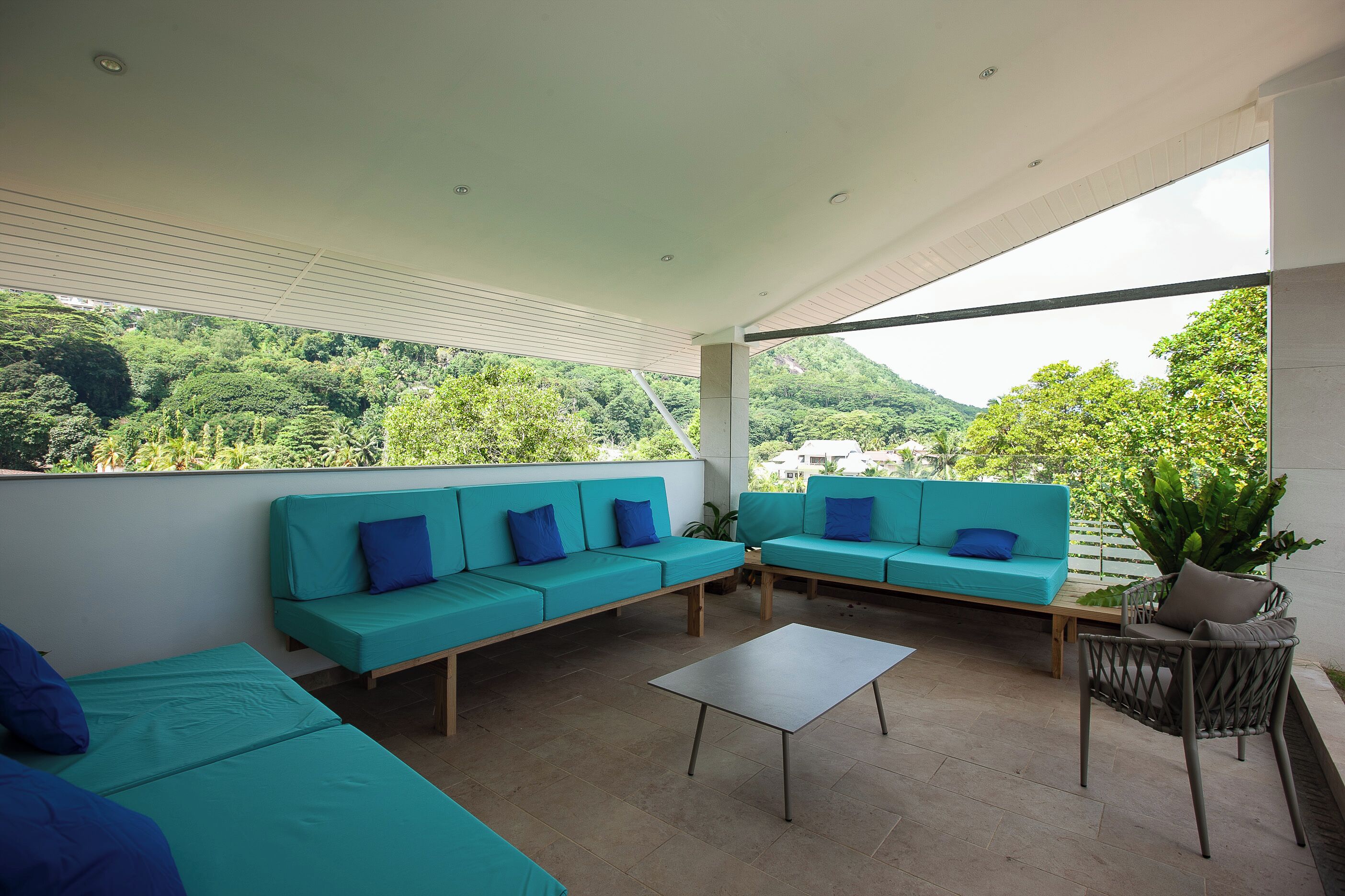 Zona relax esterna moderna con divani color petrolio e un tavolino, con vista su un paesaggio verdeggiante.