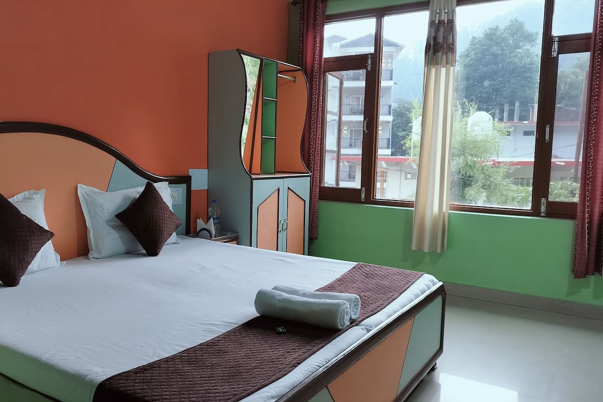 A neatly made bed with pillows, a bedside table, a wardrobe, and a window with curtains.