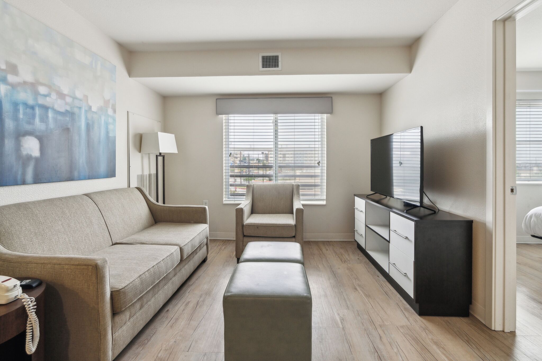 A modern living room with a sofa, armchair, ottoman, TV stand, and artwork on the wall.
