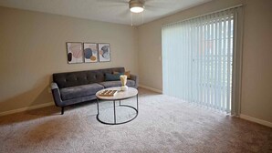 Ein Wohnzimmer mit grauem Sofa, einem runden Couchtisch und einem Deckenventilator.