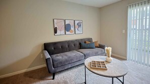 Ein Wohnzimmer mit grauem Sofa, einem runden Couchtisch und abstrakter Wandkunst.