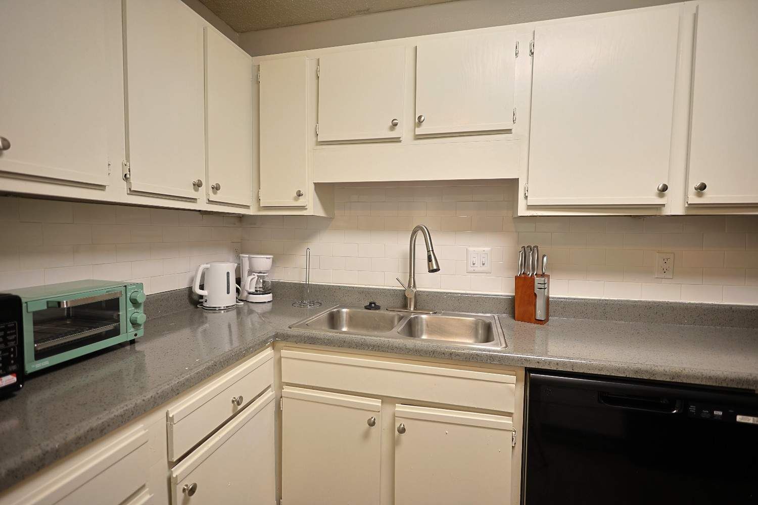 A kitchen with white cabinets, a stainless steel sink, a coffee maker, a toaster, and a knife block.
