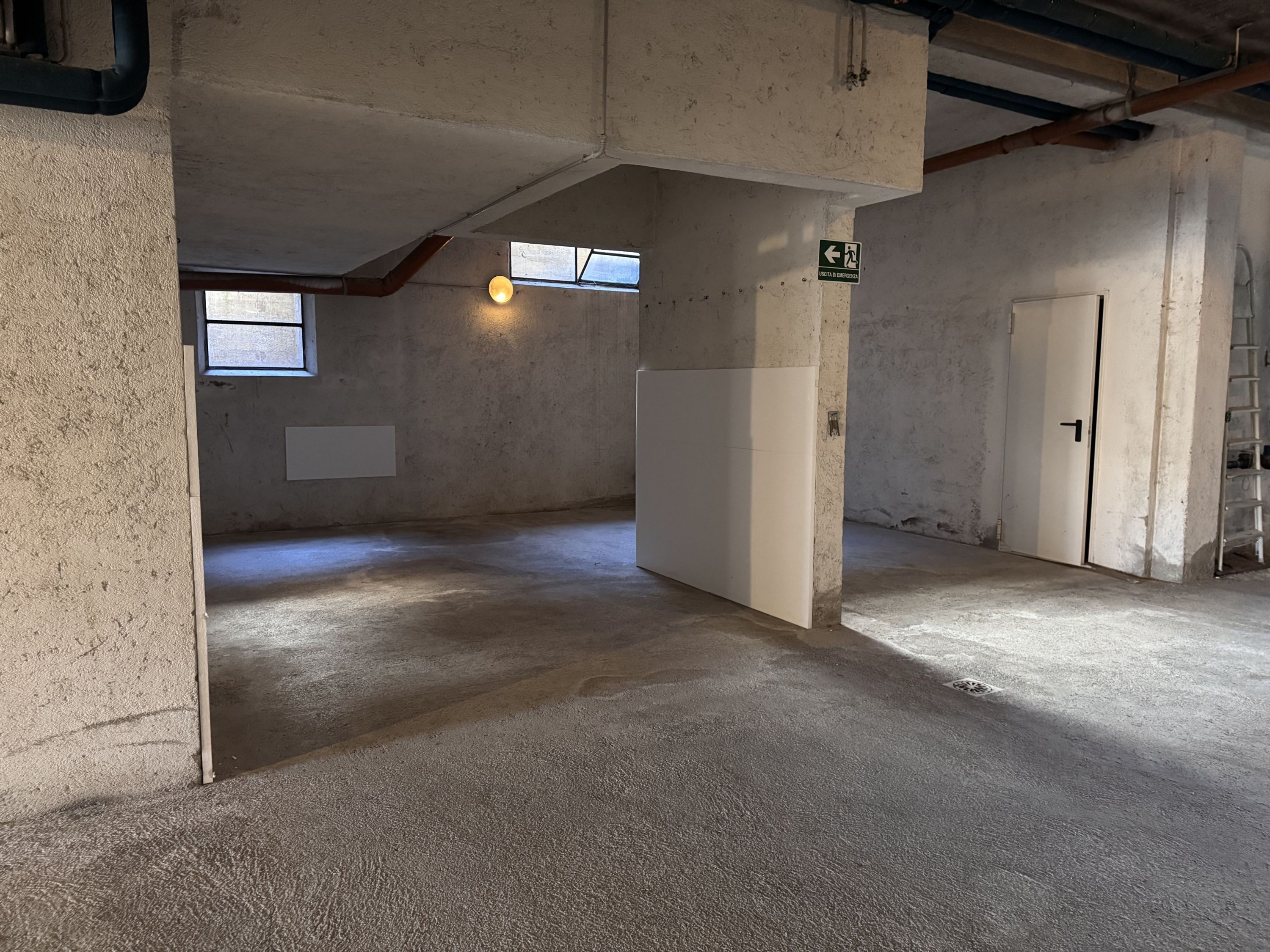 Habitación con paredes de concreto, techo inclinado y una puerta. Se ve una ventana con vistas al exterior.