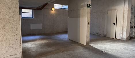 Habitación con paredes de concreto, techo inclinado y una puerta. Se ve una ventana con vistas al exterior.