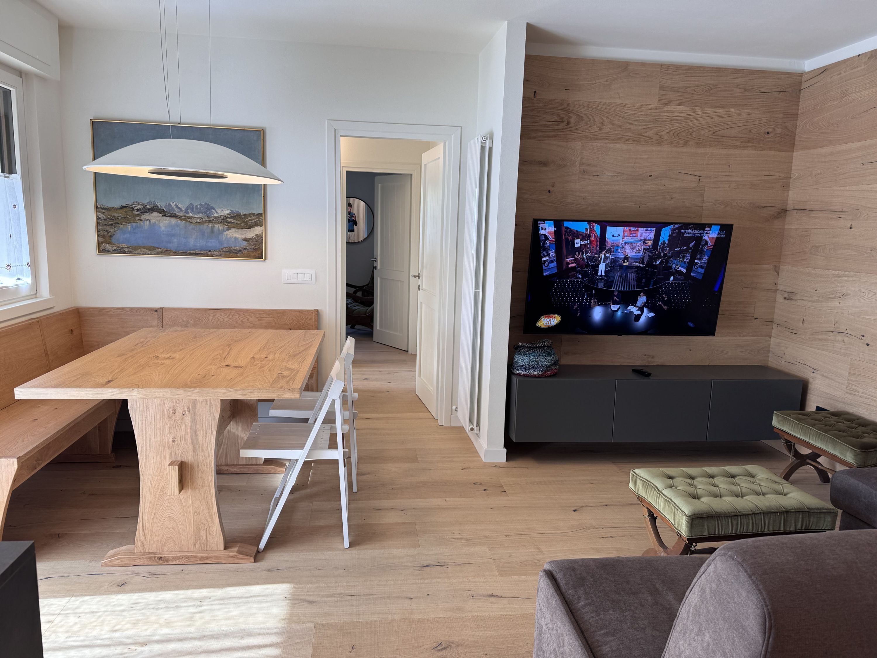 Moderni olohuone, jossa on puinen ruokapöytä, puiseen seinään asennettu televisio ja penkki.