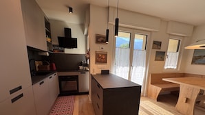 A modern kitchen with a central island, wooden flooring, and a red patterned rug. - 002 Moderno Trilocale Pinzolo (Pinzolo)