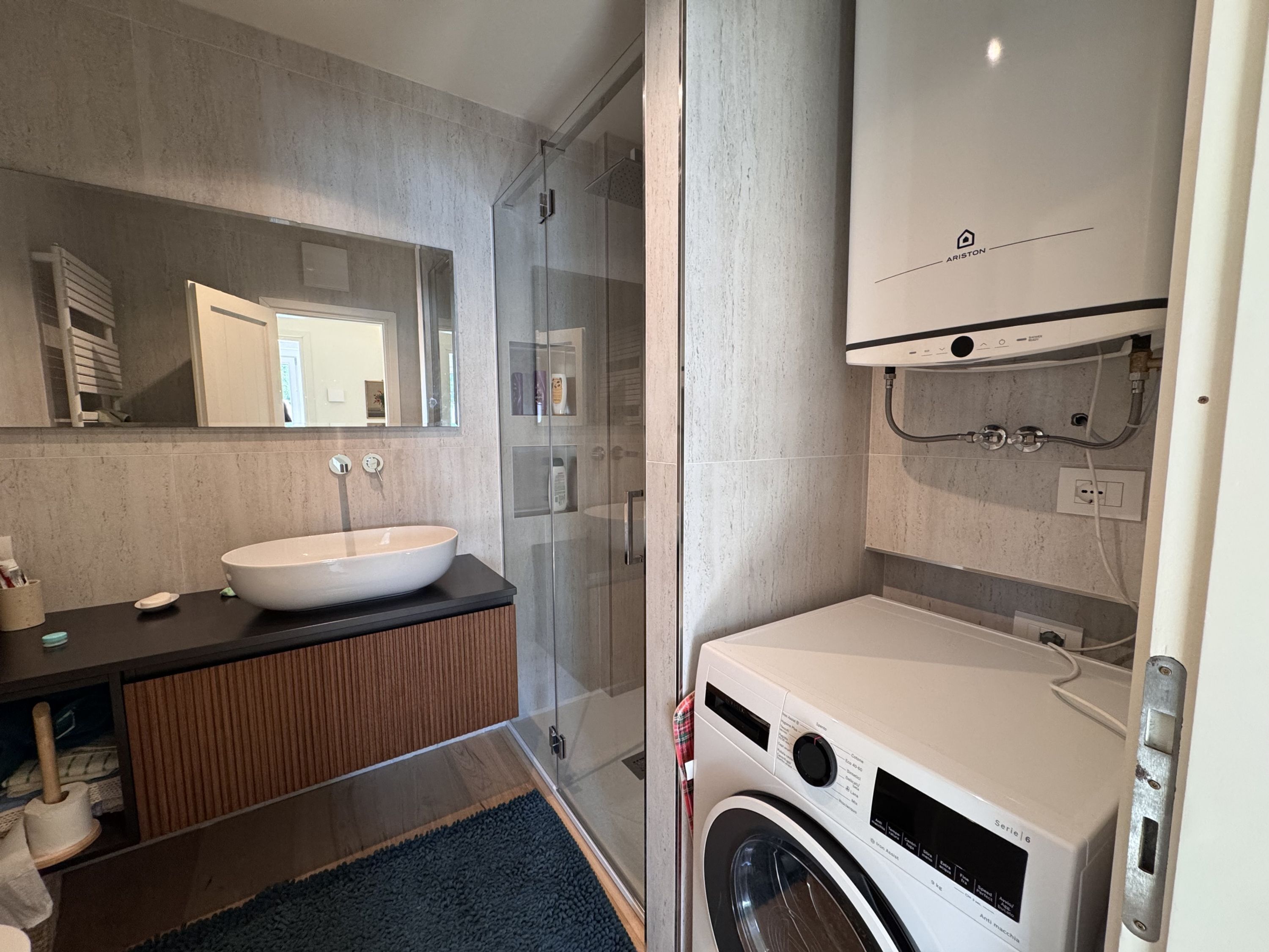Een moderne badkamer met een groot wastafel, een douchecabine van glas en een voorlaad wasmachine.