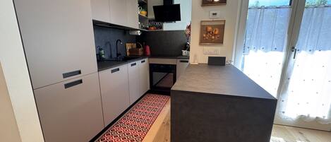 A modern kitchen with grey cabinets, a black countertop, and a red patterned rug.