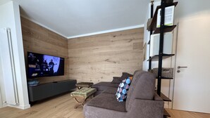 A living room with a grey sofa, a television mounted on a wooden wall, and a small wooden coffee table. - 002 Moderno Trilocale Pinzolo (Pinzolo)