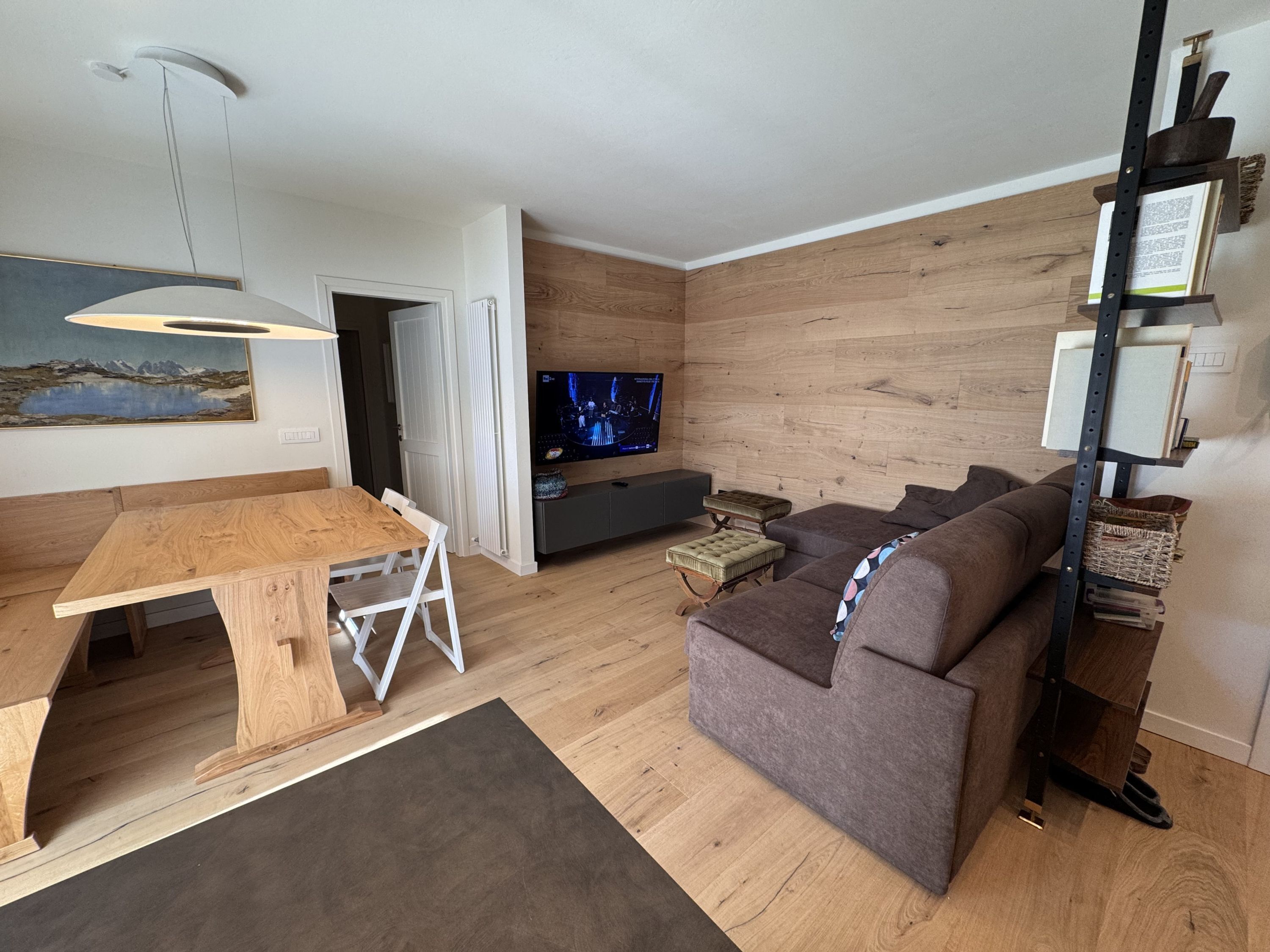 Una sala de estar moderna con una mesa de comedor de madera, un sofá gris y un televisor de pantalla plana montado en la pared.