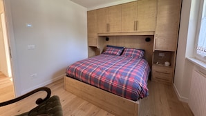 A bedroom with a wooden bed frame, a plaid bedspread, and a headboard with storage cabinets. - 002 Moderno Trilocale Pinzolo (Pinzolo)