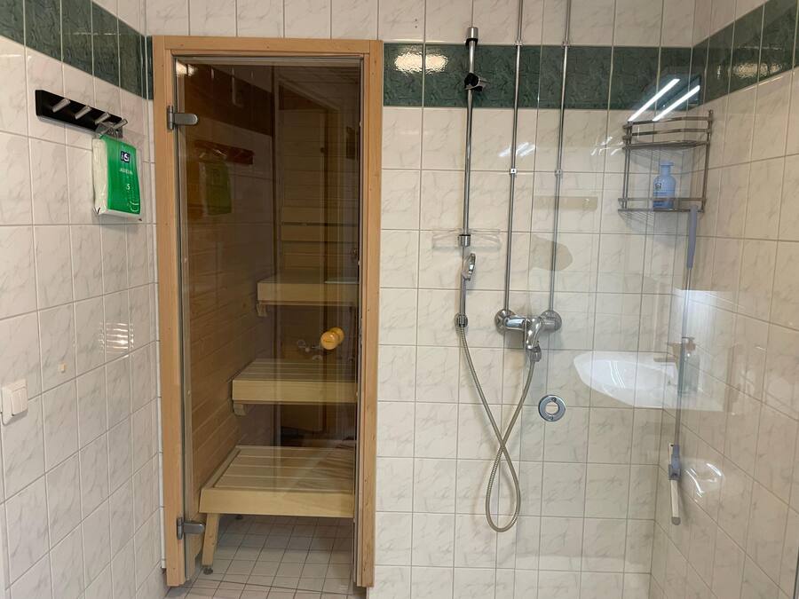 A shower area with a glass door, a sink, and a shelf with toiletries.