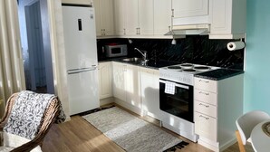 A compact kitchen with white cabinets, a microwave, a stove, and a sink. - Kotimaailma KotikaksioKirkkok saunalla (Lahti)
