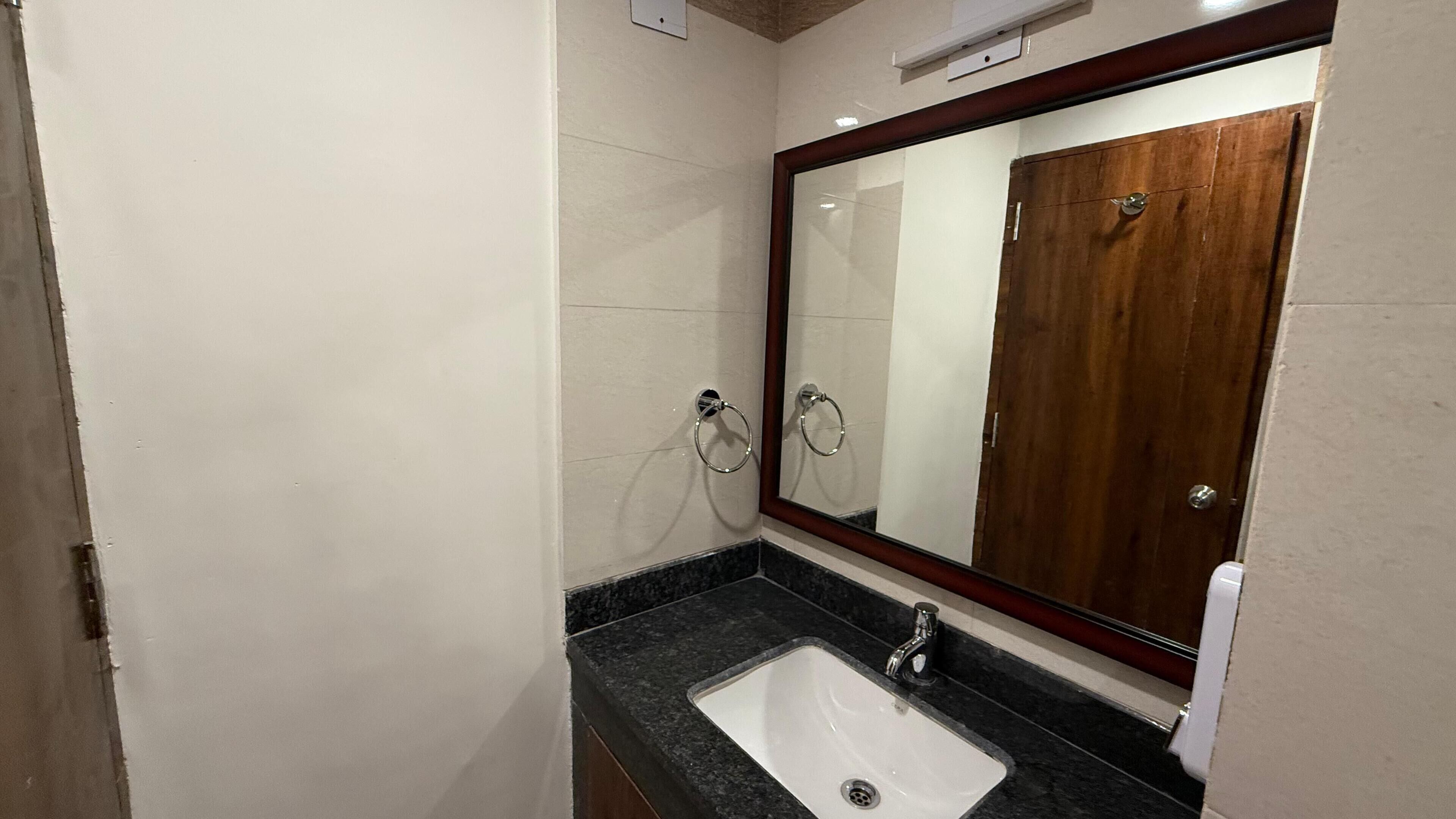 A bathroom with a white sink, a mirror with a wooden frame, and a towel ring on the wall.