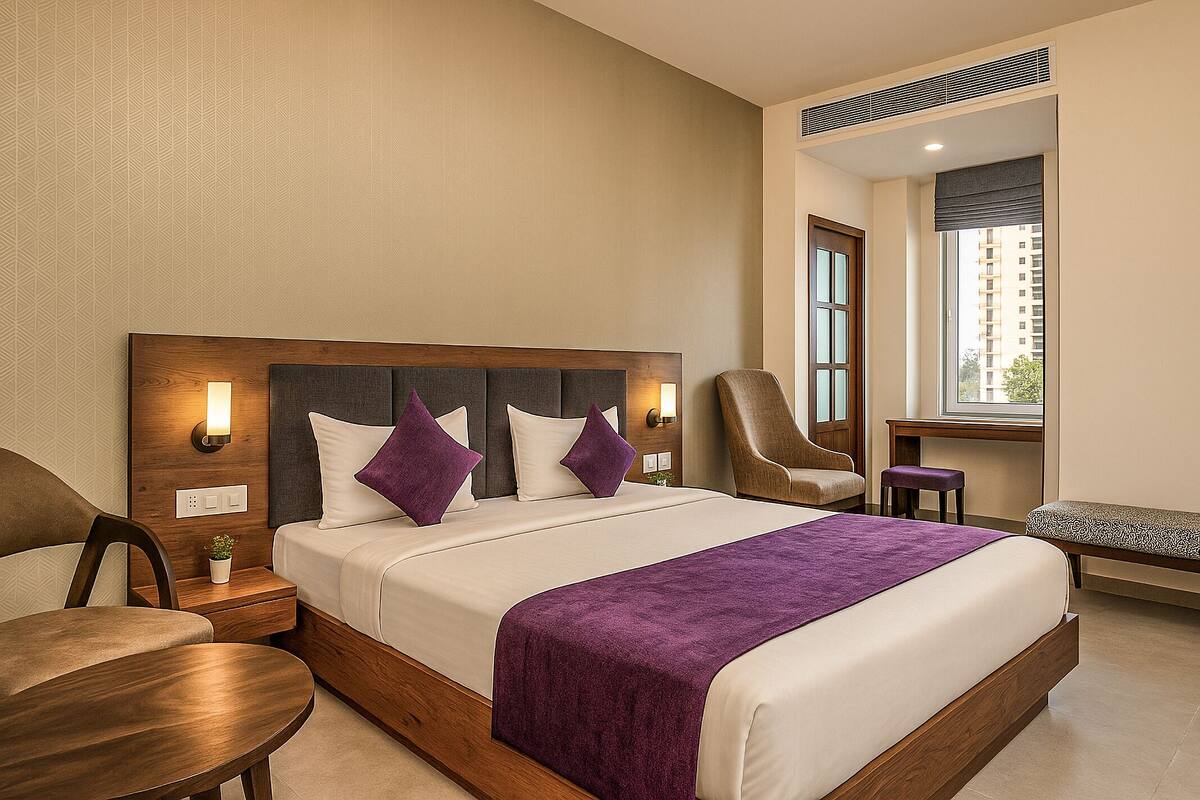 Ein Hotelzimmer mit einem großen Bett, einem Sessel, einem kleinen Tisch und einem Fenster mit Blick auf Gebäude.