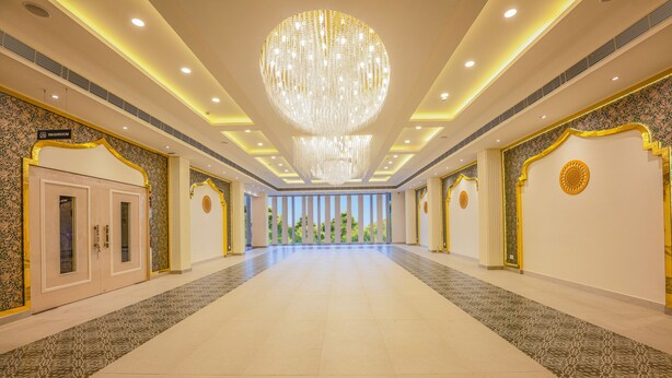 A spacious hotel lobby with a large chandelier, patterned walls, and a view of greenery through large windows. - purple leaf (Bhubaneshwar)