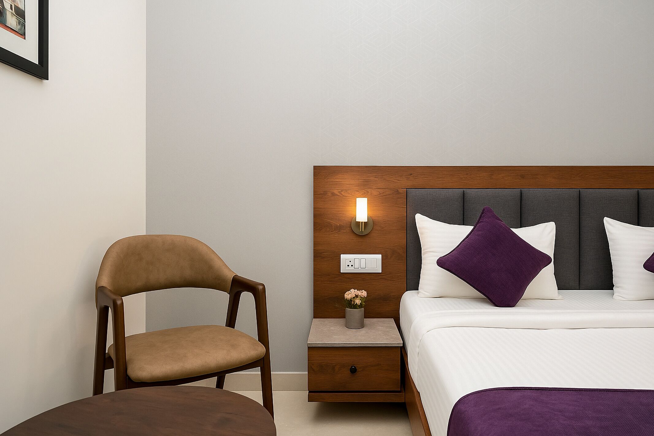 Een hotelkamer met een houten hoofdbord, een nachtkastje met een lamp, een stoel en een bed met wit en paars beddengoed.