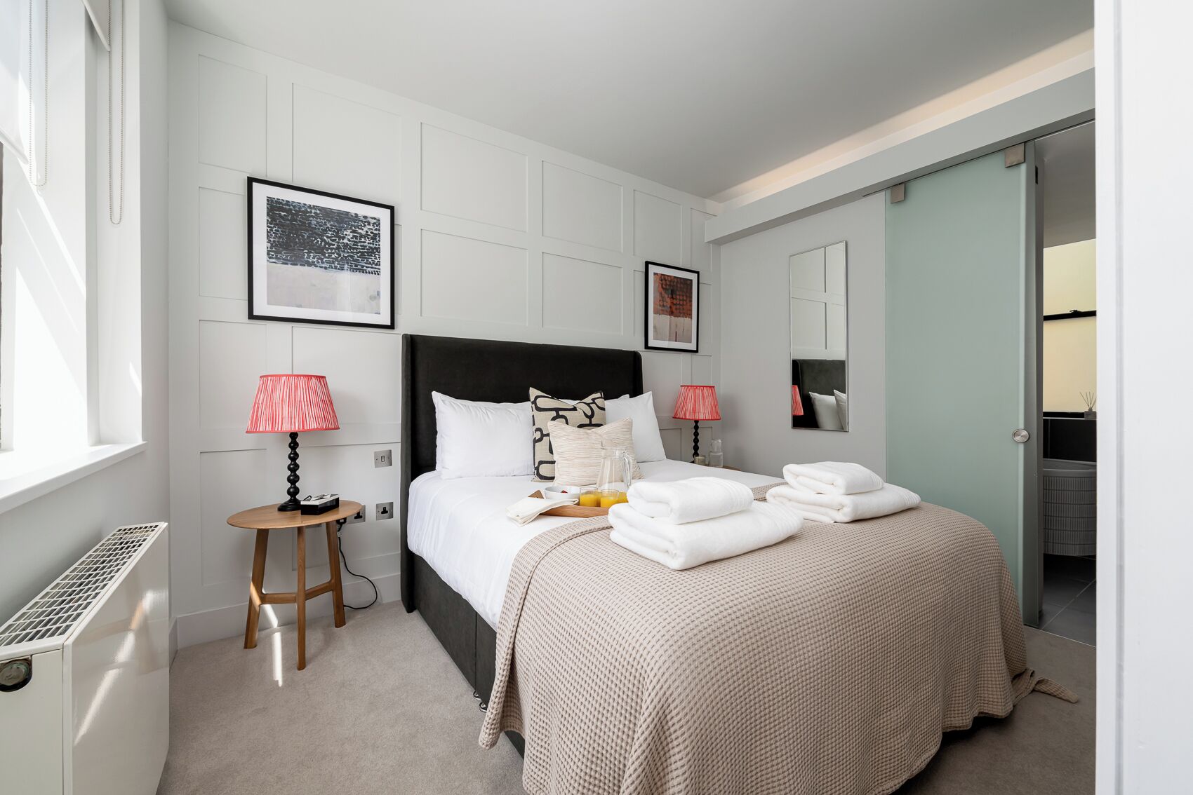 Een hotelkamer met een bed, twee bedlampen, een tafeltje, een radiator en een raam.