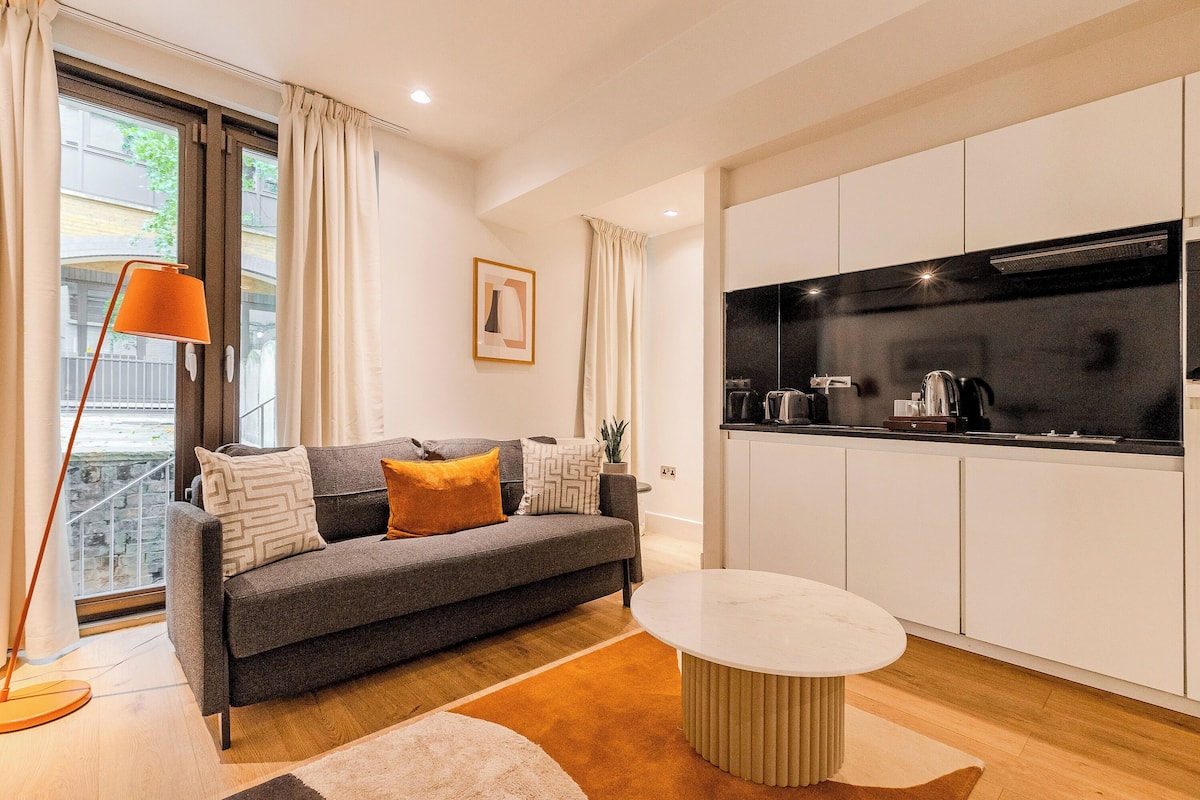 Uma sala de estar moderna com sofá, mesa de centro e área de cozinha com armários e eletrodomésticos.