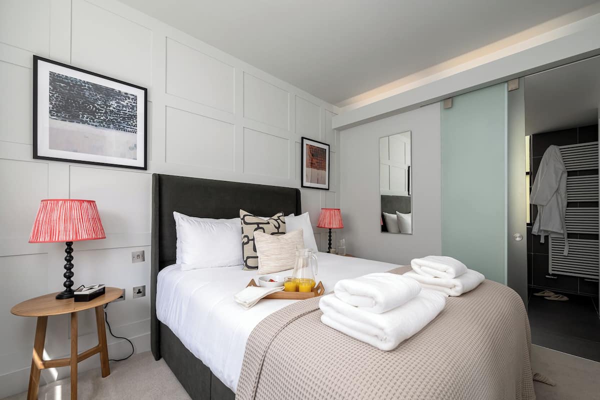 Quarto de hotel com cama, mesas de cabeceira, espelho e banheiro visível através de uma porta aberta.