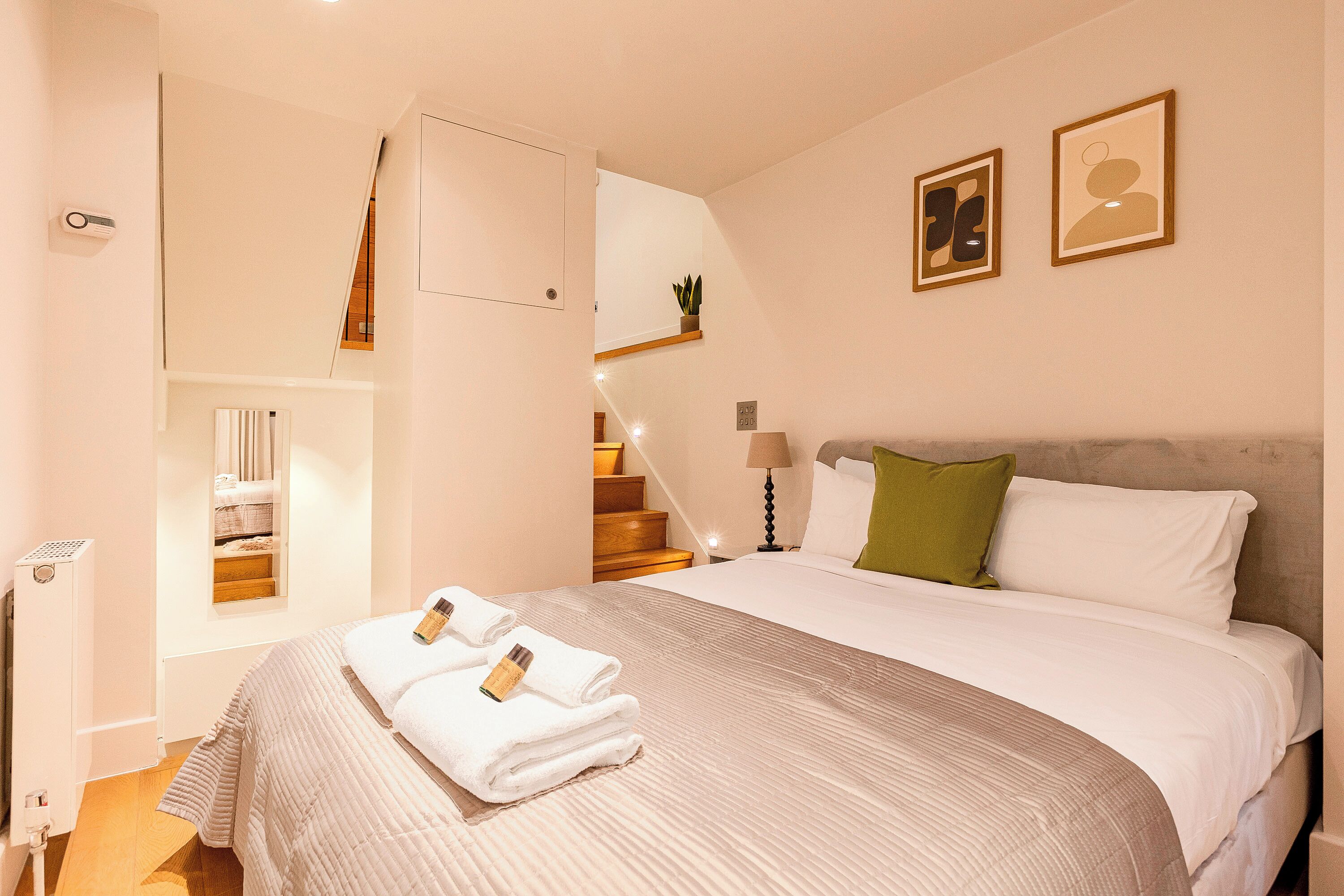 A hotel room with a bed, a nightstand, a lamp, a green pillow, and a framed picture on the wall.