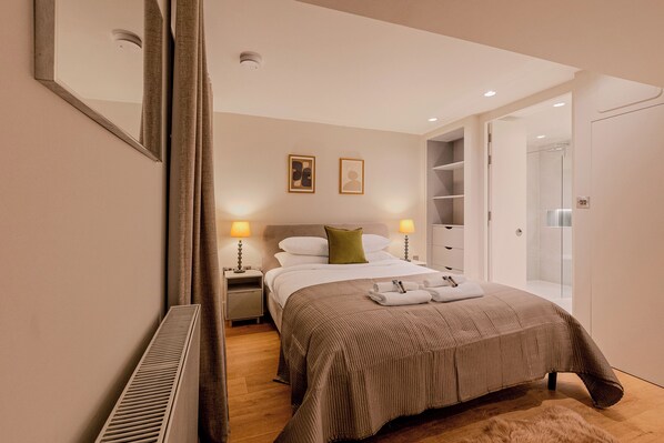 Quarto de hotel com cama, abajures, espelho, radiador e guarda-roupa.