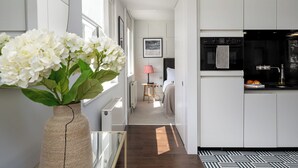 A modern kitchen with white cabinetry and a black oven. A vase with white flowers is on a table in the foreground. - Your Apartment - St. Paul's (London)