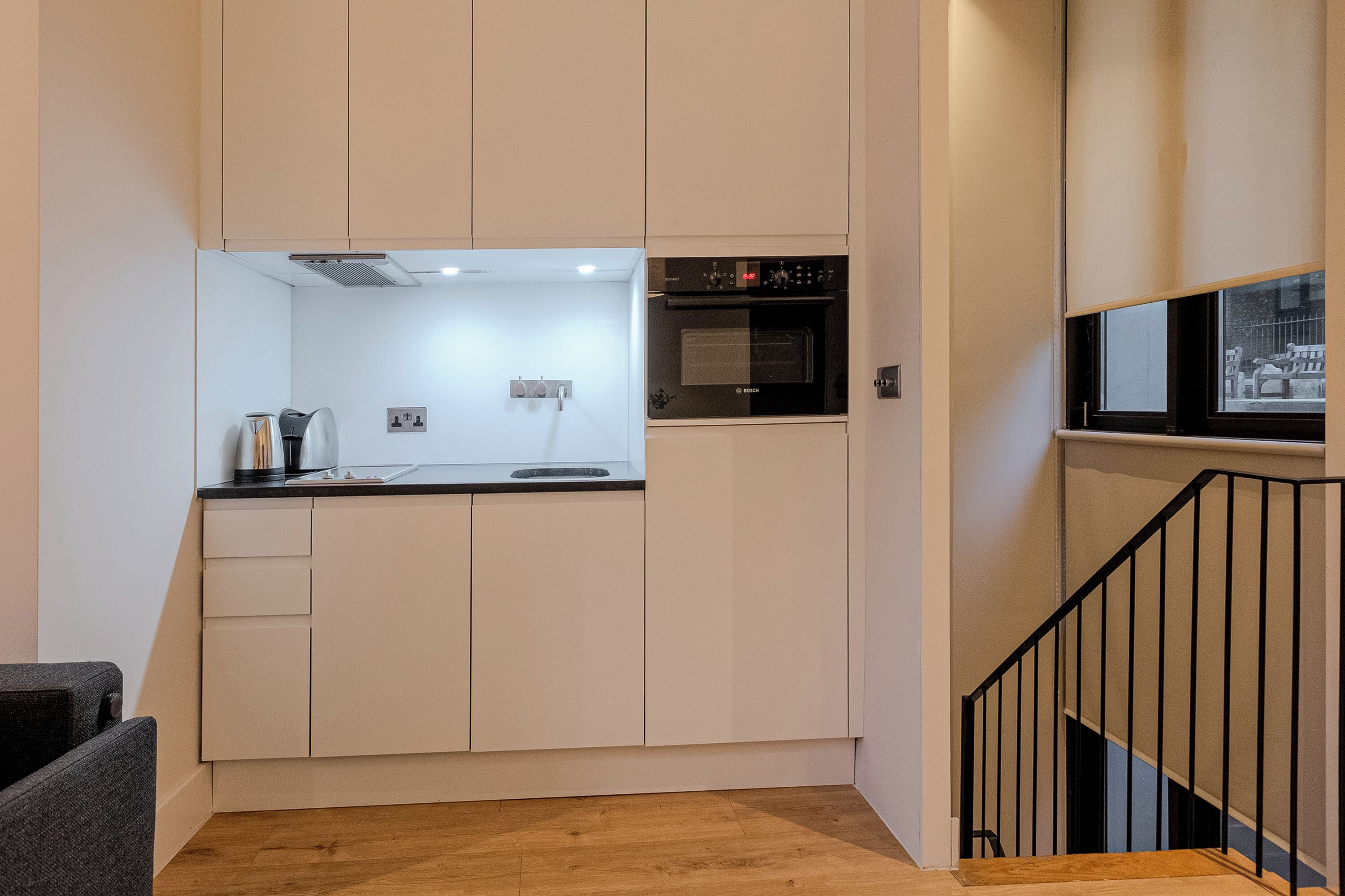 A compact kitchen with white cabinets, a black oven, and a wooden floor.