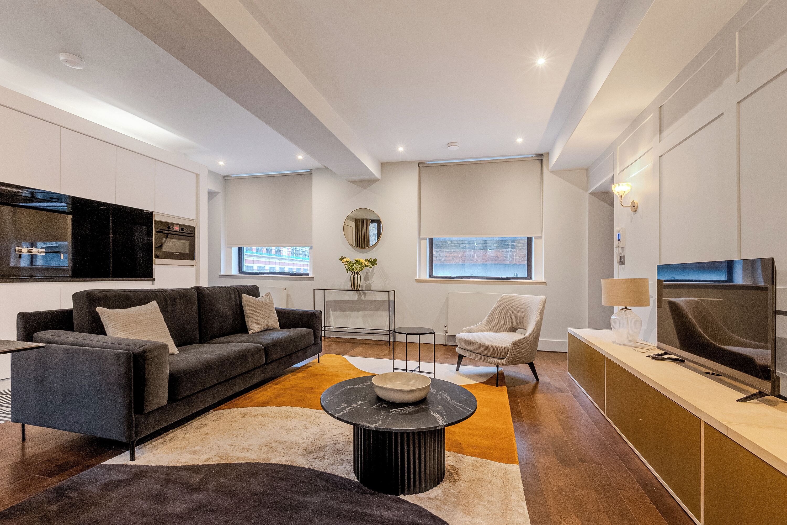 A modern living room with a sofa, armchair, coffee table, TV, and a view of the city.