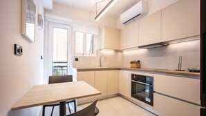 A modern kitchen with a dining area, featuring a built-in oven, a window, and a light fixture. - Stylish 1BR in Pangrati | Balcony & Green View (Athina)
