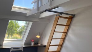 Ein Schlafzimmer im Loft-Stil mit Dachfenstern, einer Holzleiter, einem Schreibtisch und einem Stuhl.