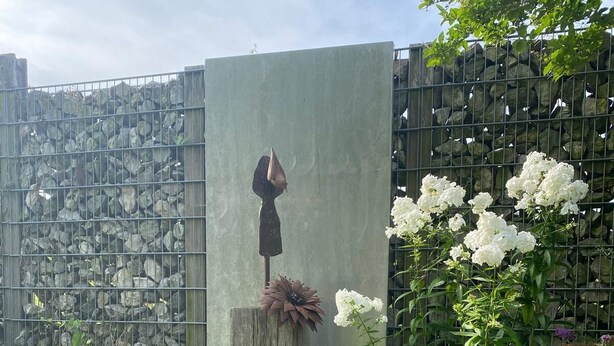 Ein Gartenbereich mit einem Betonpflanzgefäß, einer Vogelstatue und weißen Blüten.