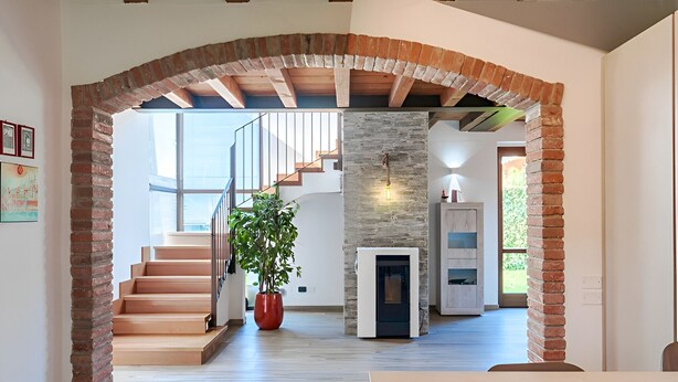 A spacious interior with a wooden staircase, a fireplace, and a large window providing natural light.