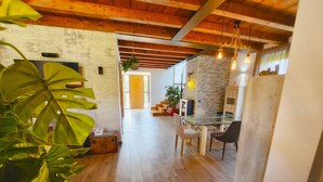 A spacious room with wooden floors, a glass table, and chairs. There is a potted plant in the foreground.