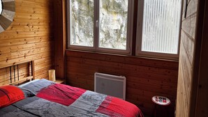 A wooden room with a bed, a heater, and a window with blinds. - Comfortable 44m² apartment, Eaux-Bonnes, close to ski resorts and hiking trails (Eaux-Bonnes)