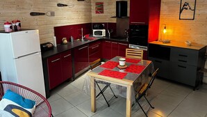 A compact kitchen with wooden walls, a dining table with red placemats, and a red chair. - Comfortable 44m² apartment, Eaux-Bonnes, close to ski resorts and hiking trails (Eaux-Bonnes)