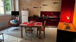 A modern kitchen with wooden panel walls, a dining area with a table and chairs, and a red accent wall. - Comfortable 44m² apartment, Eaux-Bonnes, close to ski resorts and hiking trails (Eaux-Bonnes)