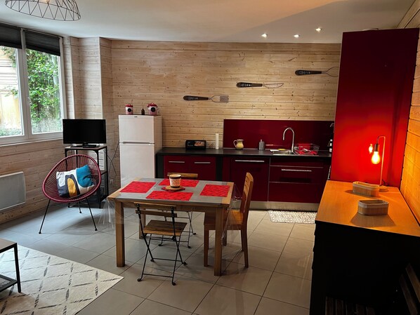 A modern kitchen with wooden panel walls, a dining area with a table and chairs, and a red accent wall. - Spacious 44-square-meter apartment in Eaux-Bonnes, near ski resorts and hiking trails (Eaux-Bonnes)