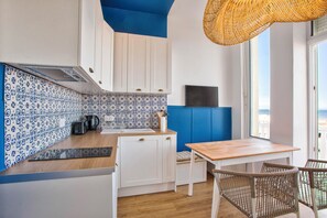 A modern kitchen with white cabinets, blue patterned backsplash, and a wooden table with wicker chairs. - Bleu Horizon - Studio with balcony and sea view (Villers-sur-Mer)