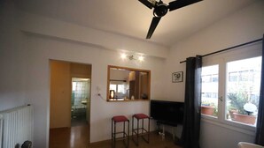 Un saló amb un ventilador de sostre, una televisió, dos tamborets vermells, un mirall gran i vistes a l'exterior per una finestra.