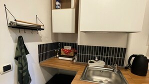 A compact kitchen with a sink, a small black trash bin, a wooden shelf, and a towel hanging on the wall. - Casa Amicitia Spanish Steps (Roma)