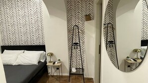 A bedroom with a bed, a small desk, a mirror, and a herringbone-patterned wall. - Casa Amicitia Spanish Steps (Roma)