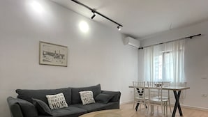 Una sala moderna con un sofá gris, un tapete rojo, una mesa de centro de madera y un comedor con sillas blancas y una mesa.
