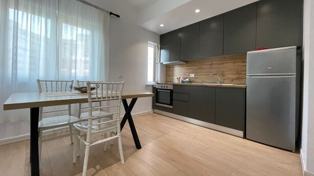 Una cocina moderna con armarios oscuros, un refrigerador de acero inoxidable y una encimera de madera.